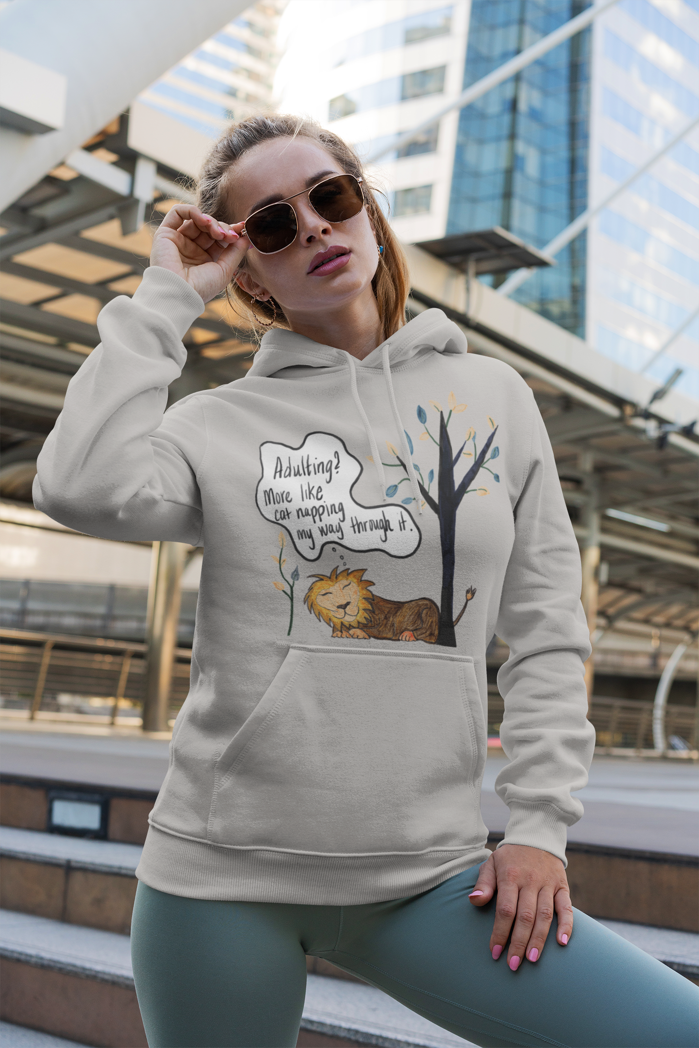 Woman wearing carbon grey Adulting Nap Lion hoodie adjusting sunglasses – funny adulting cat nap design by GrungePup Sarcastic Affirmations