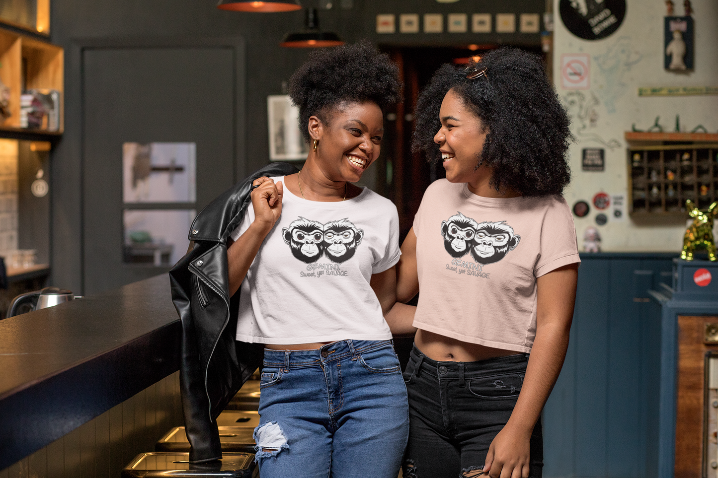 Woman and woman standing together, each wearing a Gemini Sweet Yet Savage cropped tee — one white and one orchid