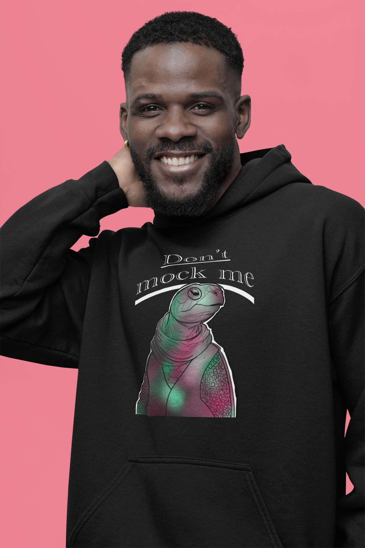 Smiling bearded man wearing a black Gildan hoodie with the Don’t Mock Me design against a pink background