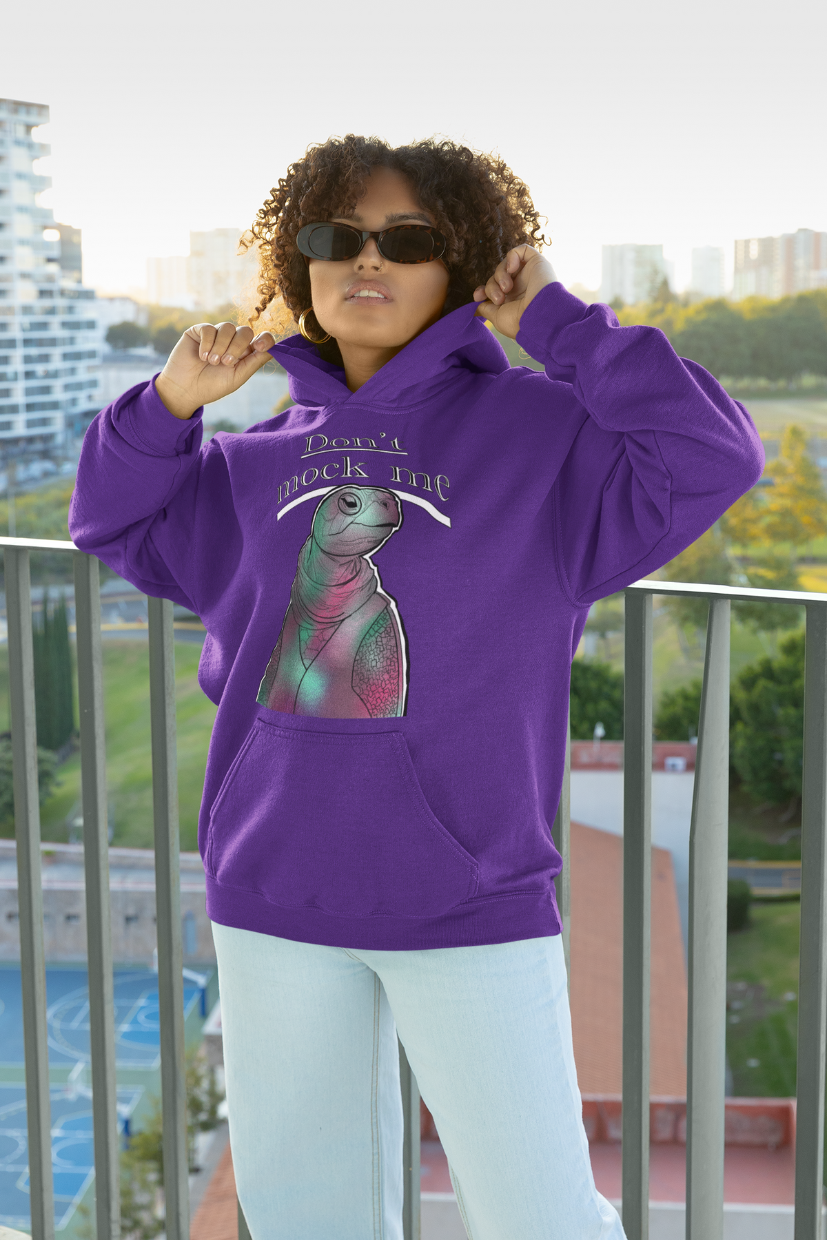 Curly-haired woman posing with sunglasses and adjusting her hoodie while wearing a purple Gildan hoodie featuring the Don’t Mock Me design