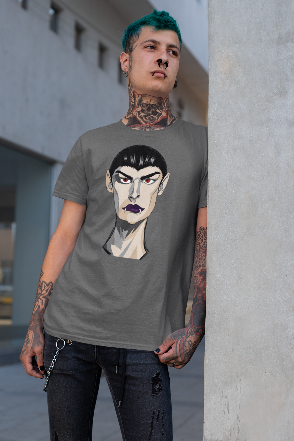 Tattooed man with green hair leaning against a concrete wall wearing an asphalt gray t-shirt printed with the Emo Vamp vampire face.