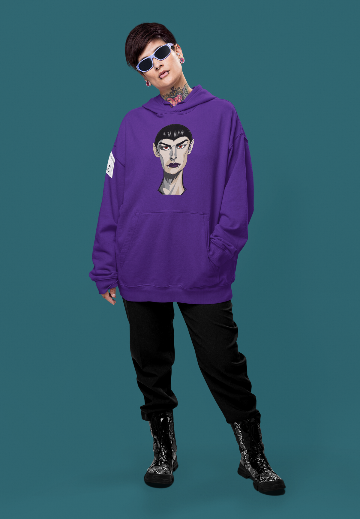 Tattooed woman in sunglasses wearing a purple hoodie printed with the Emo Vamp vampire face against a teal background.