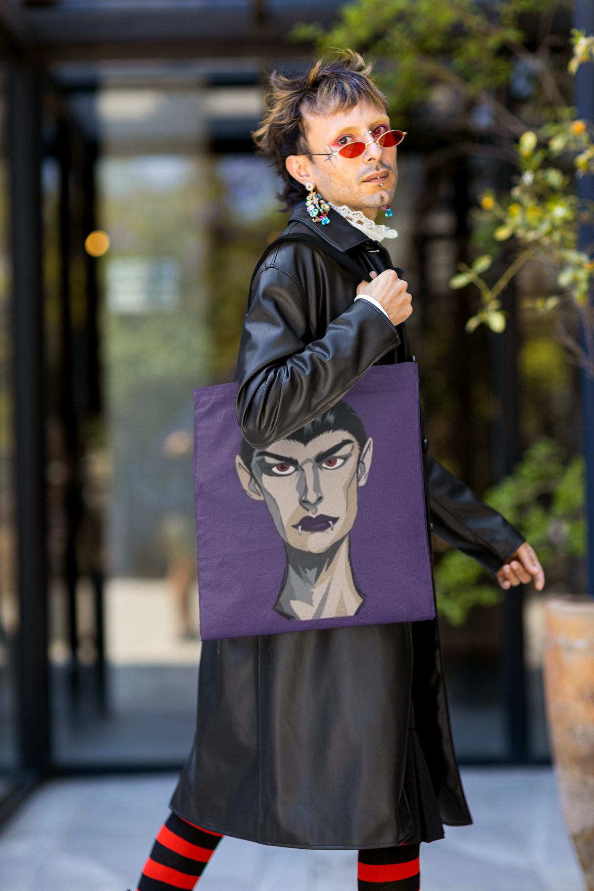 Man in a black leather coat and red sunglasses carrying a purple tote bag printed with the Emo Vamp vampire face.