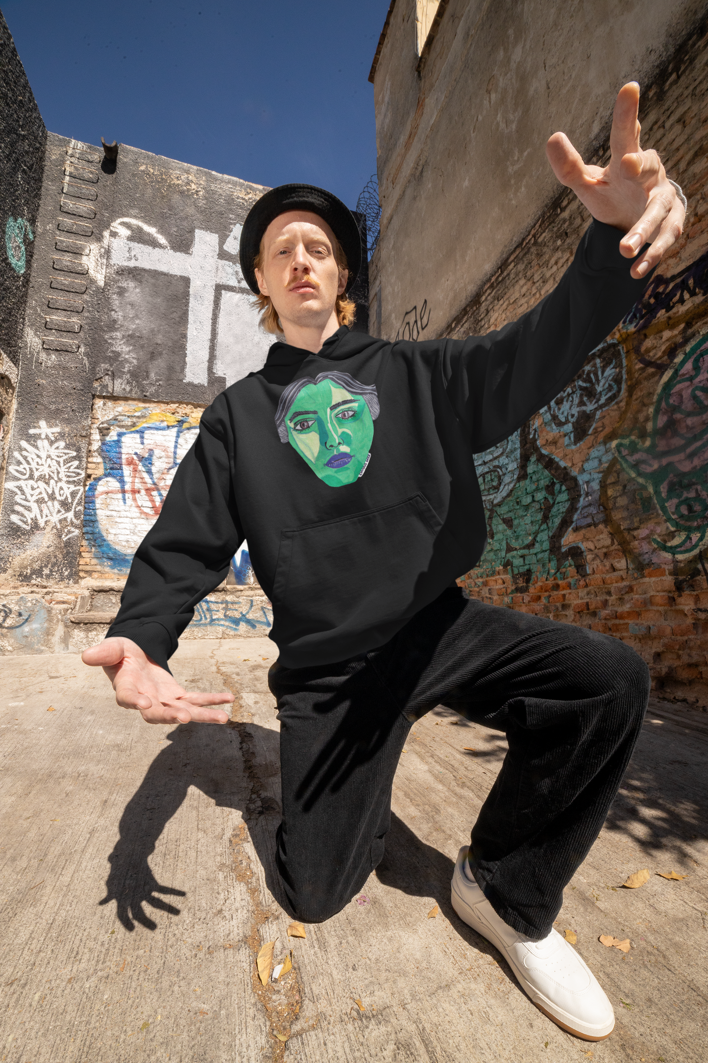 Man in black Envious Gaze hoodie doing dynamic pose with green face artwork in gritty urban setting