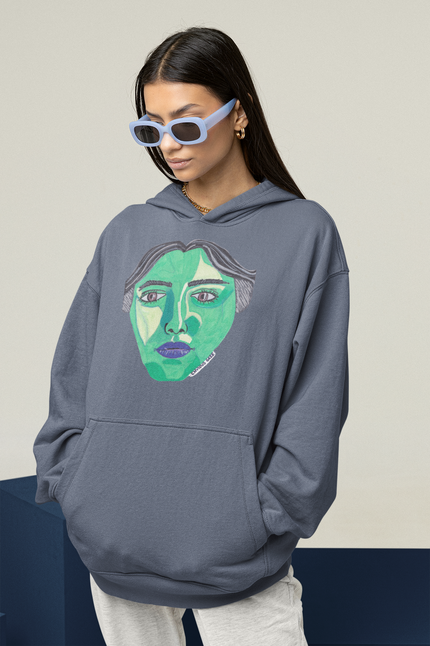 Woman in dark navy Envious Gaze hoodie with striking face artwork posing confidently in studio