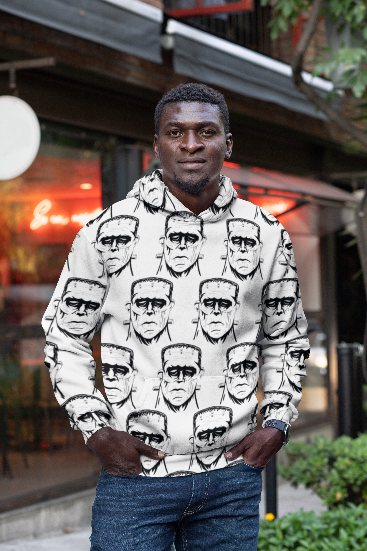 Man wearing Frank's Monster all-over print hoodie with hands in pockets standing outdoors