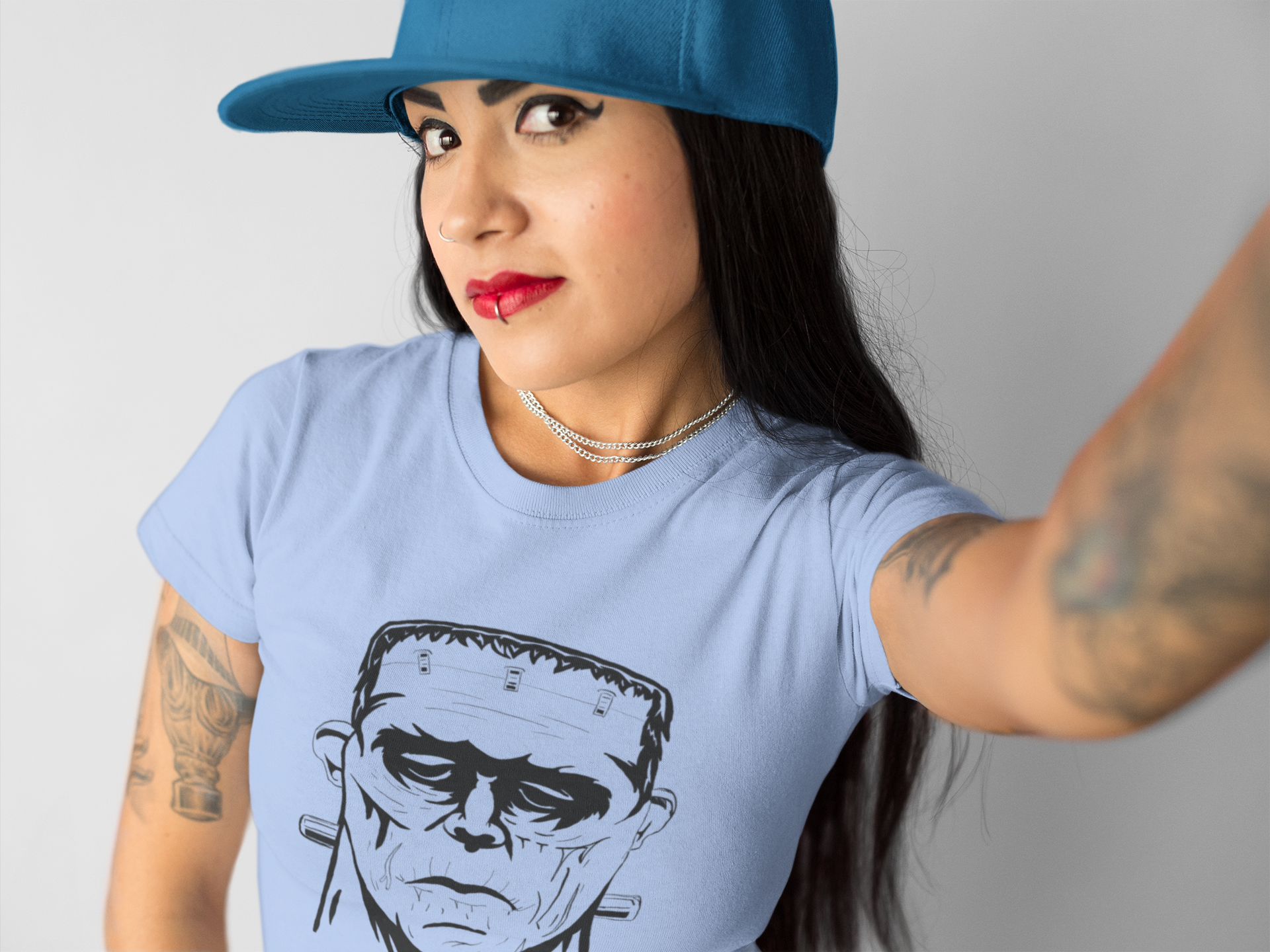 Woman wearing blue baseball cap and heather carolina blue Frank's Monster t-shirt with black and white Frankenstein illustration