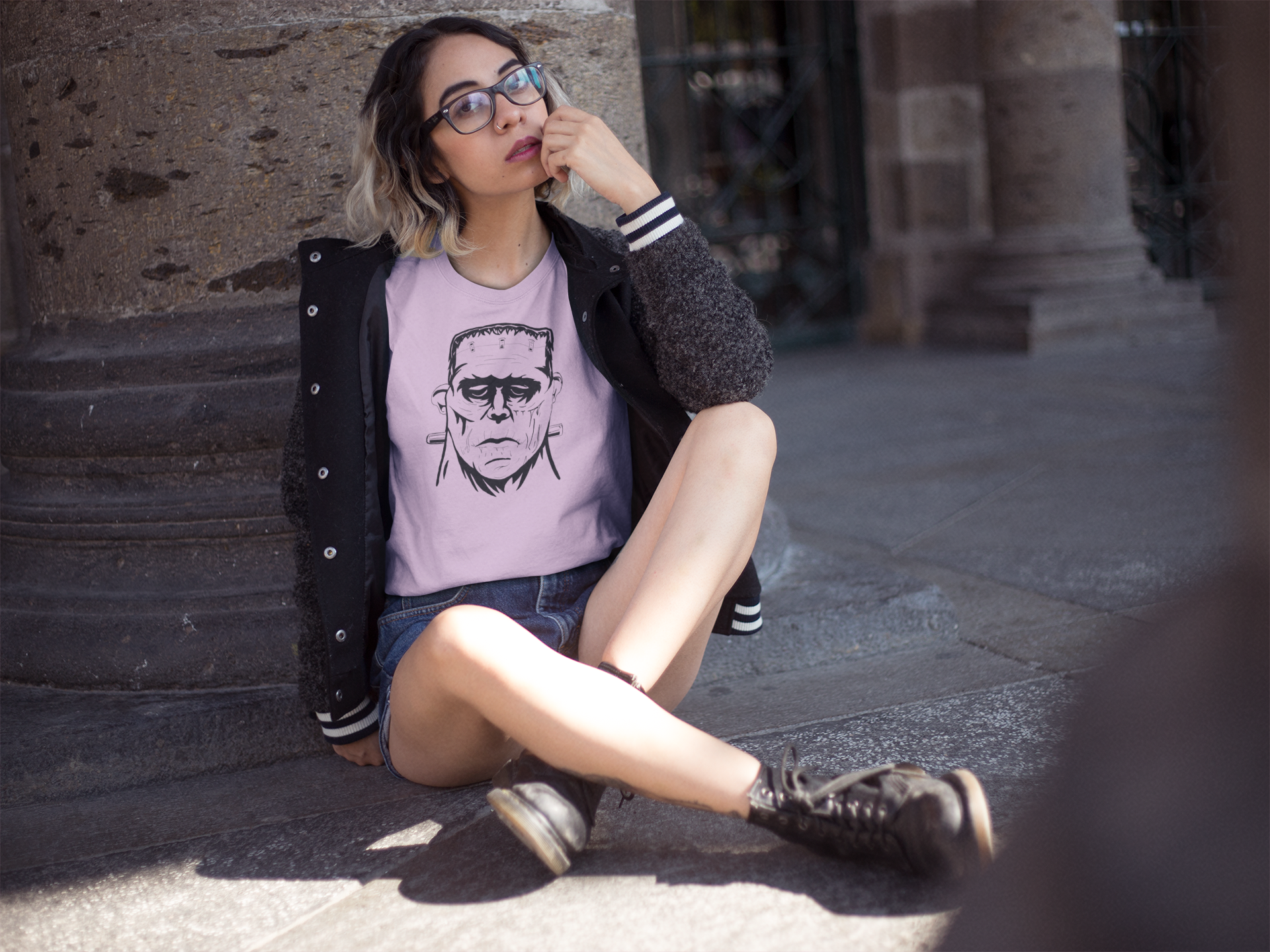 Woman sitting outdoors wearing heather prism lilac Frank's Monster t-shirt with repeating Frankenstein face design