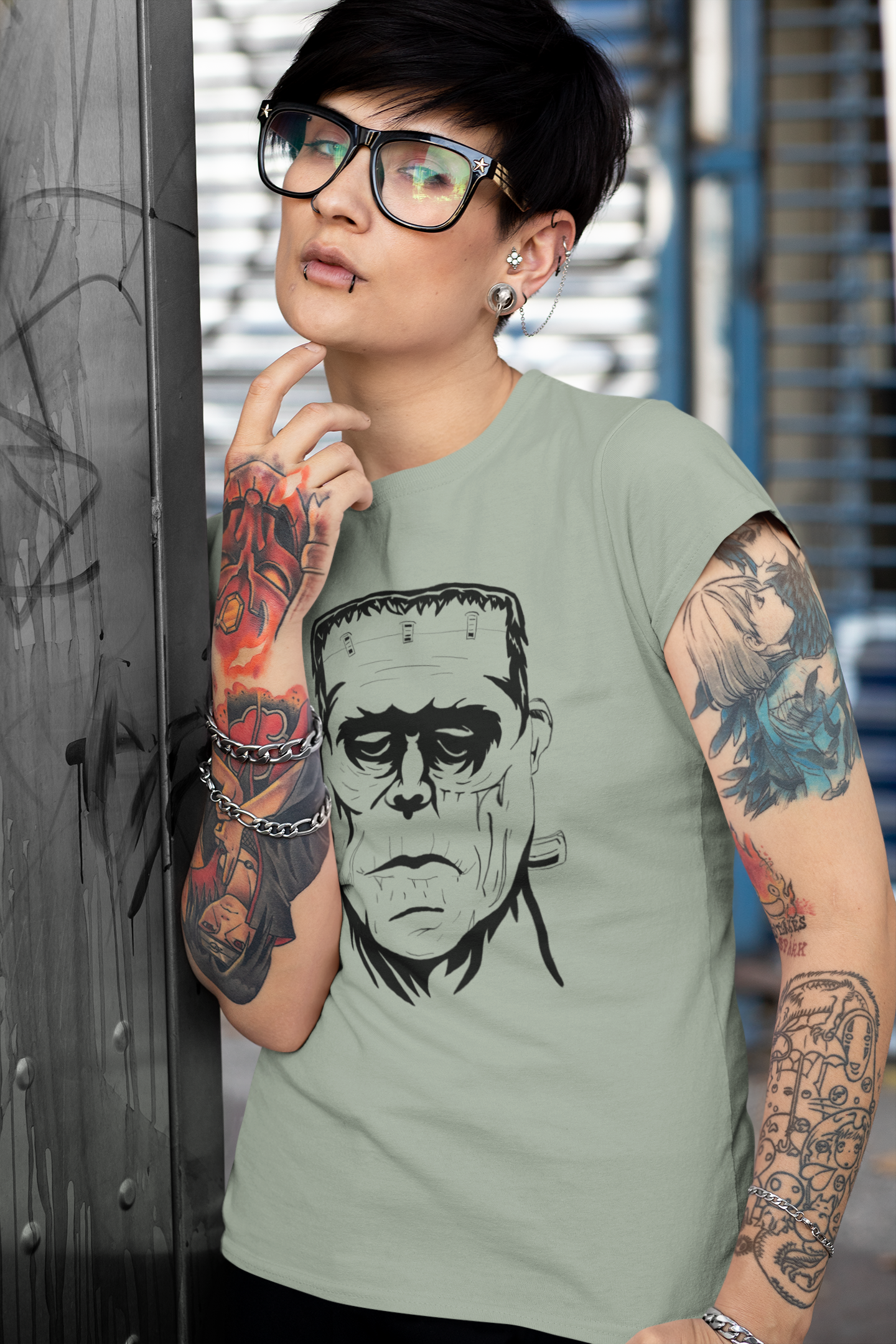 Androgynous person wearing sage green Frank's Monster t-shirt with repeating monster face pattern