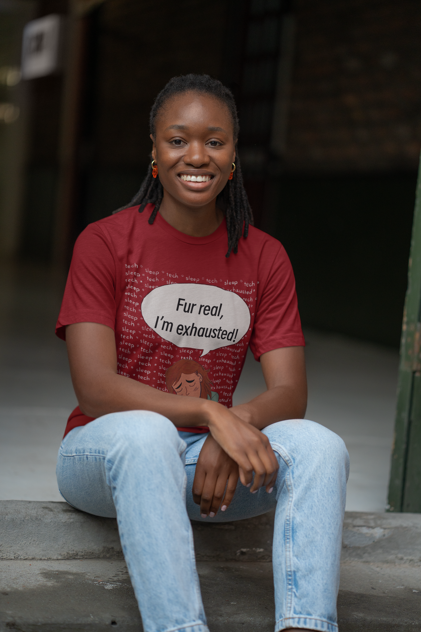 Happy woman sitting on floor in cardinal red Bella Canvas t-shirt with "Fur Real, I'm Exhausted" colorful vet tech design. Sarcastic self-care message for tired but dedicated animal care workers.