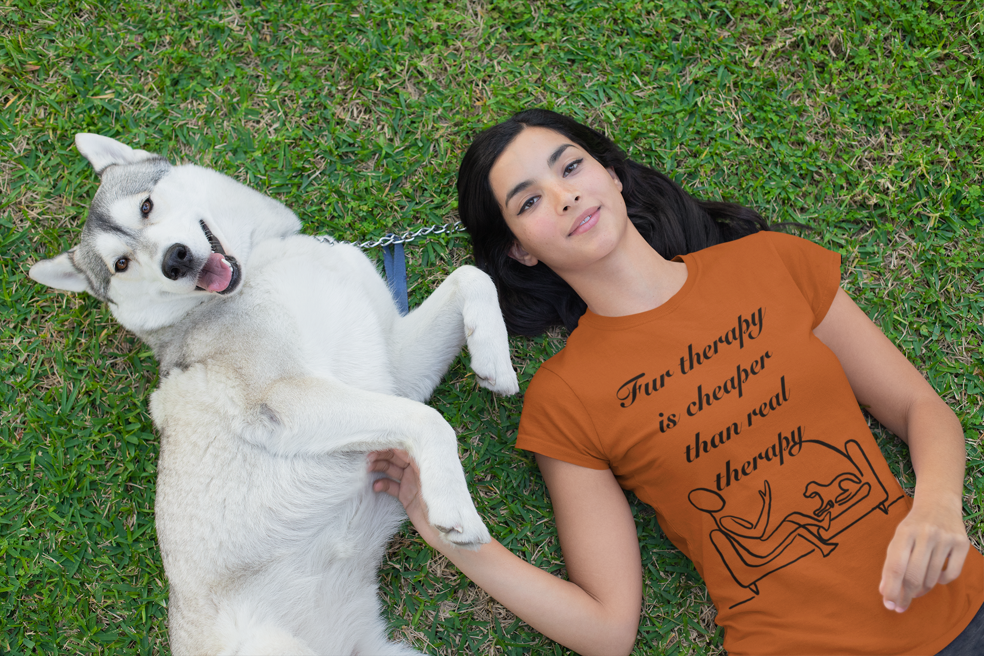 Woman lying on grass smiling with her husky while wearing autumn colored Fur Therapy t-shirt