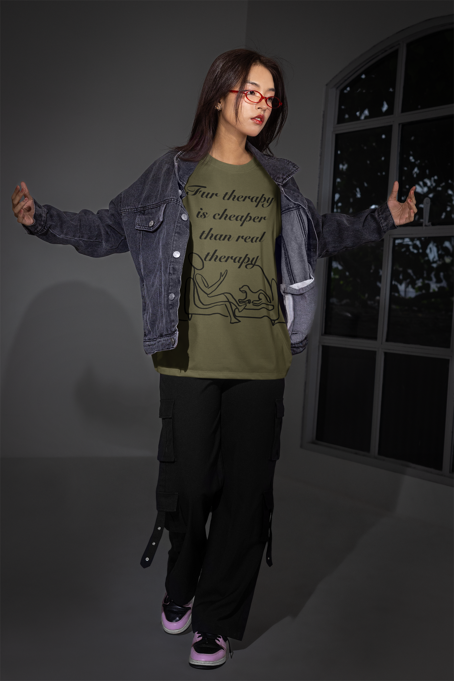 Woman in heather olive t-shirt and denim jacket posing with arms out in studio setting