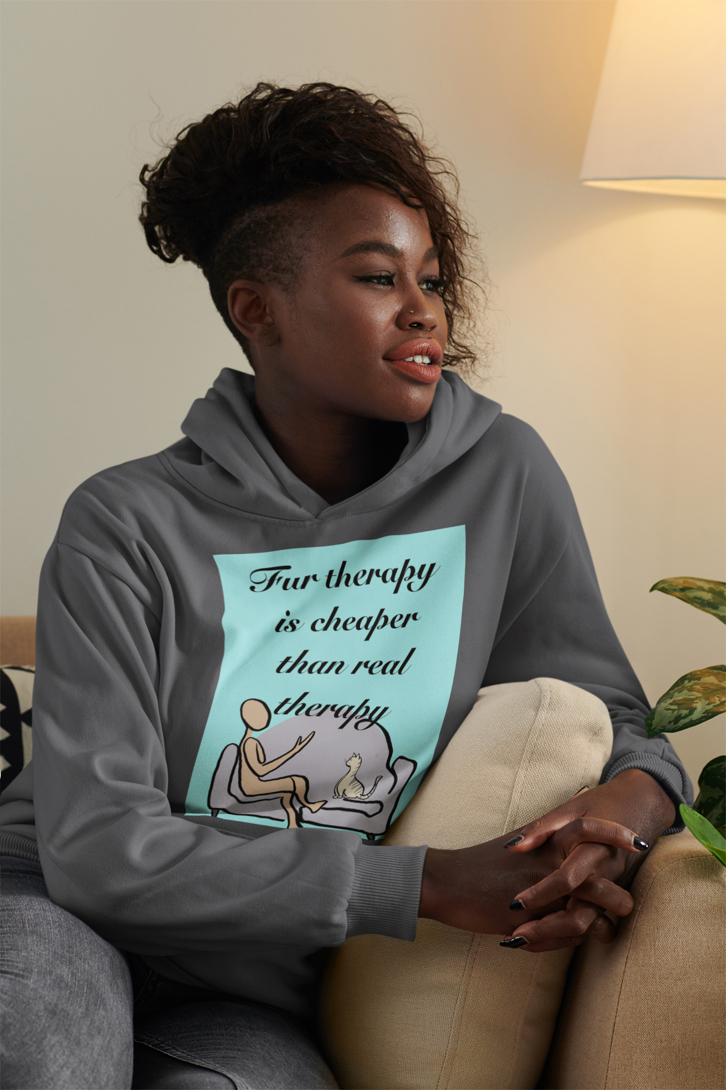 Woman with afro hairstyle wearing dark heather Fur Therapy Is Cheaper Than Real Therapy colored cat hoodie, sitting on couch – sarcastic affirmation design by GrungePup Sarcastic Affirmations