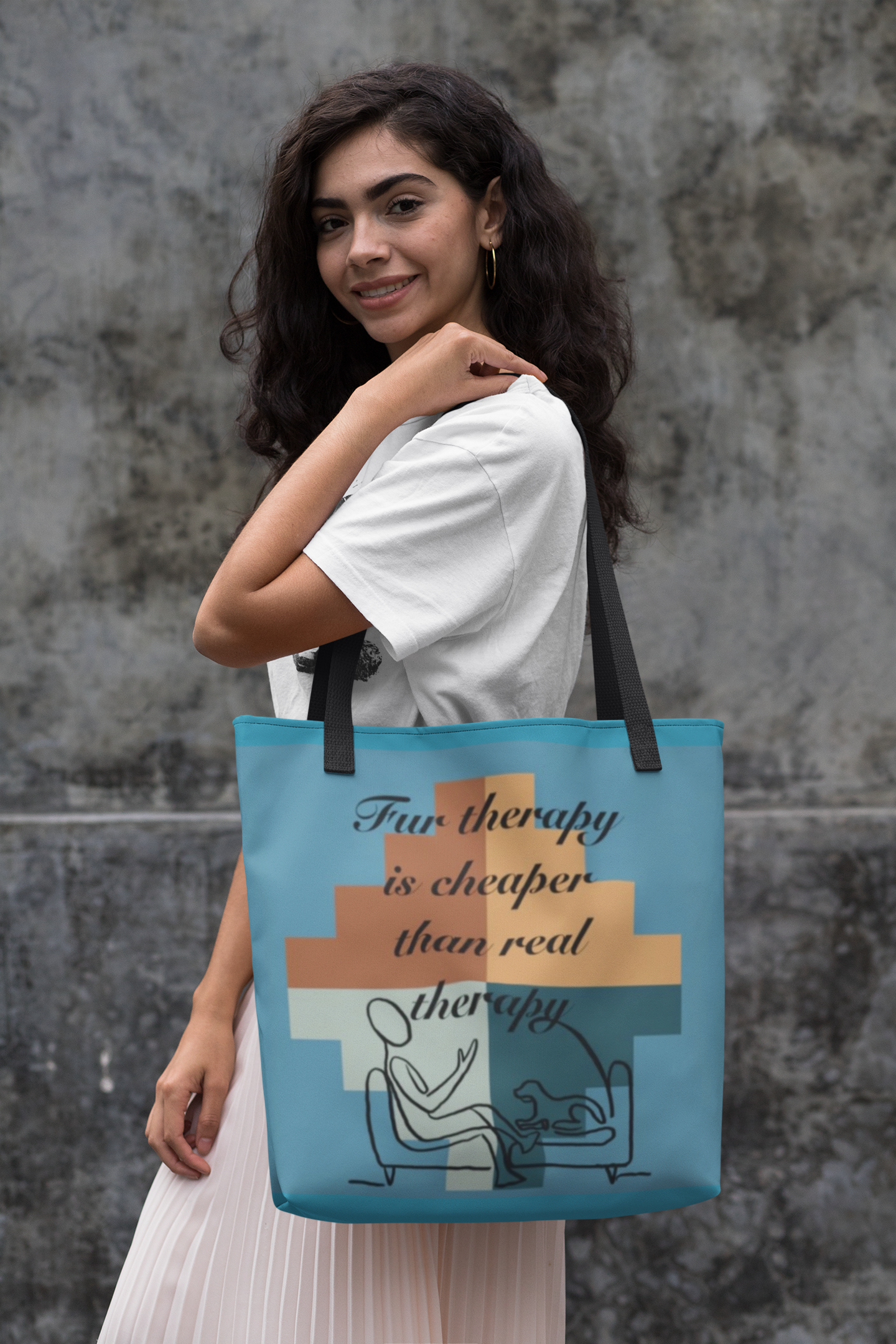 Smiling woman with long dark wavy hair holding the turquoise colored Fur Therapy is Cheaper Than Real Therapy tote bag over her shoulder against a concrete wall