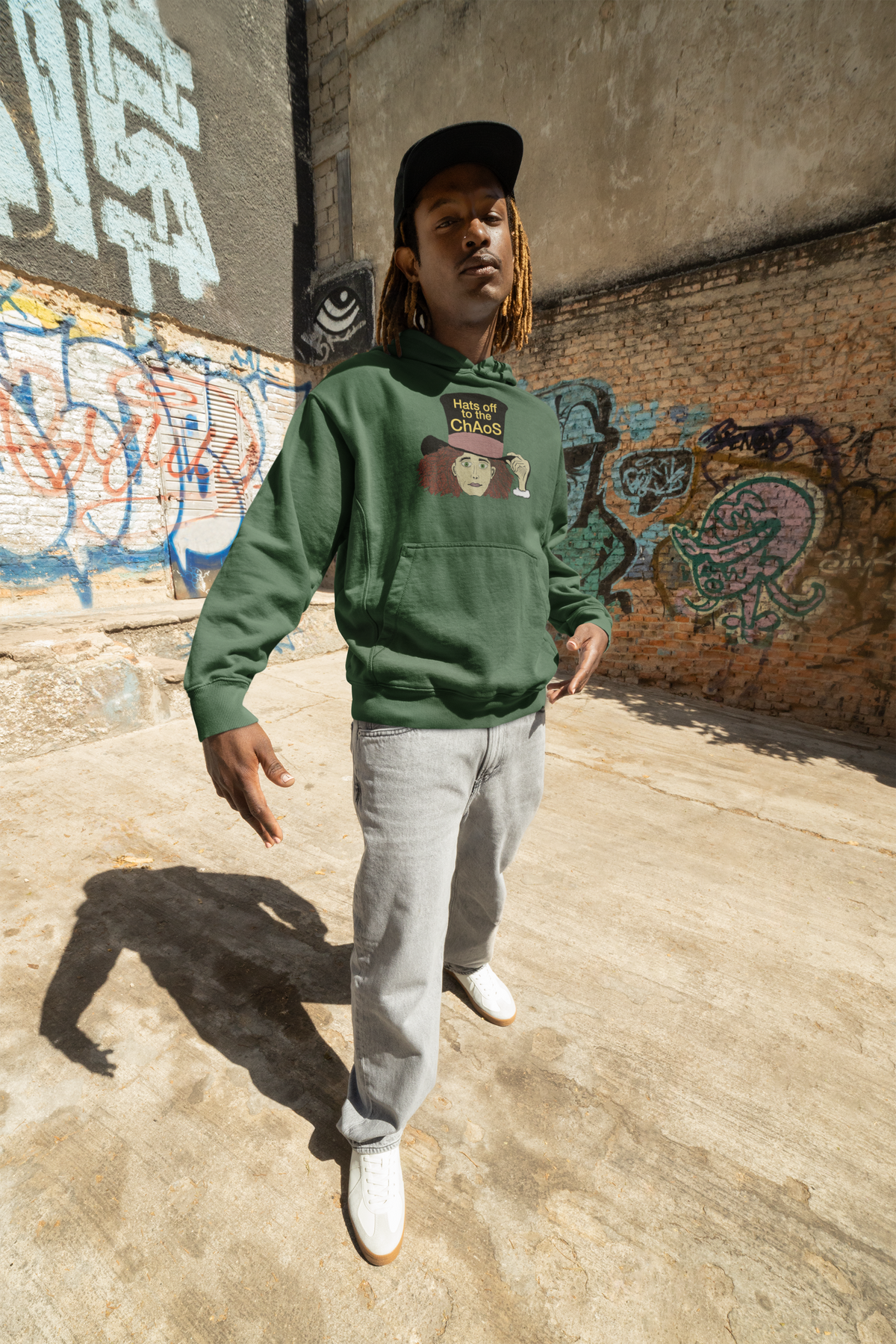 Man in a black cap and forest green Hats Off to the Chaos Mad Hatter hoodie standing in a graffiti alley. That Girl, Alice by GrungePup Gallery.