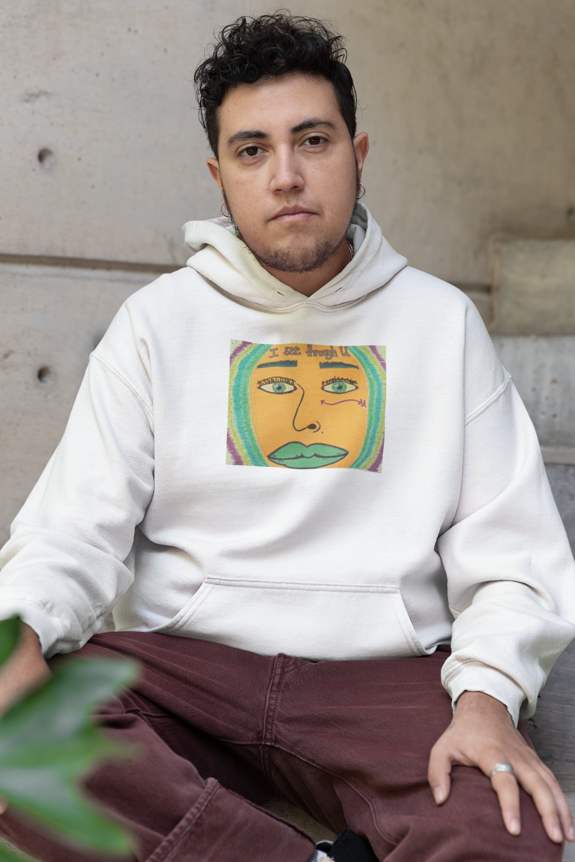Man with curly hair wearing white I See Through U hoodie sitting outdoors