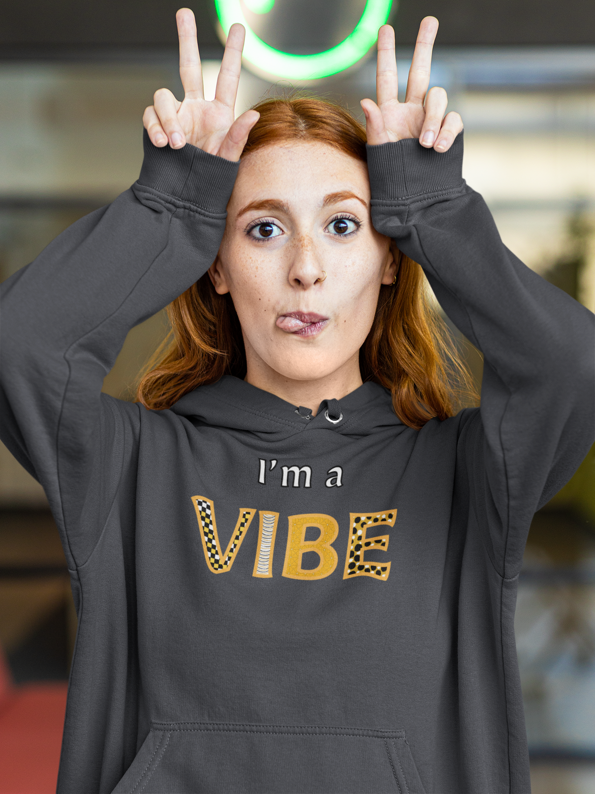 Woman in the dark heather grey I'm a Vibe hoodie makes a funny face with both hands up.
