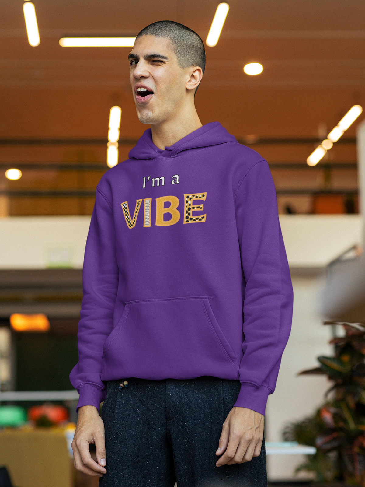 Man in the purple I'm a Vibe hoodie pulls a funny face indoors.