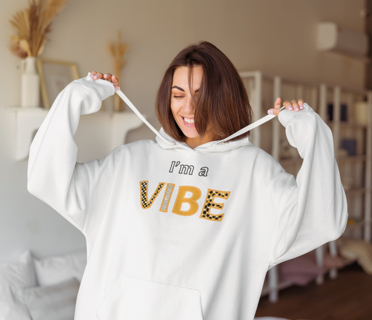 Smiling woman in the white I'm a Vibe hoodie pulls the drawstrings out to the sides.