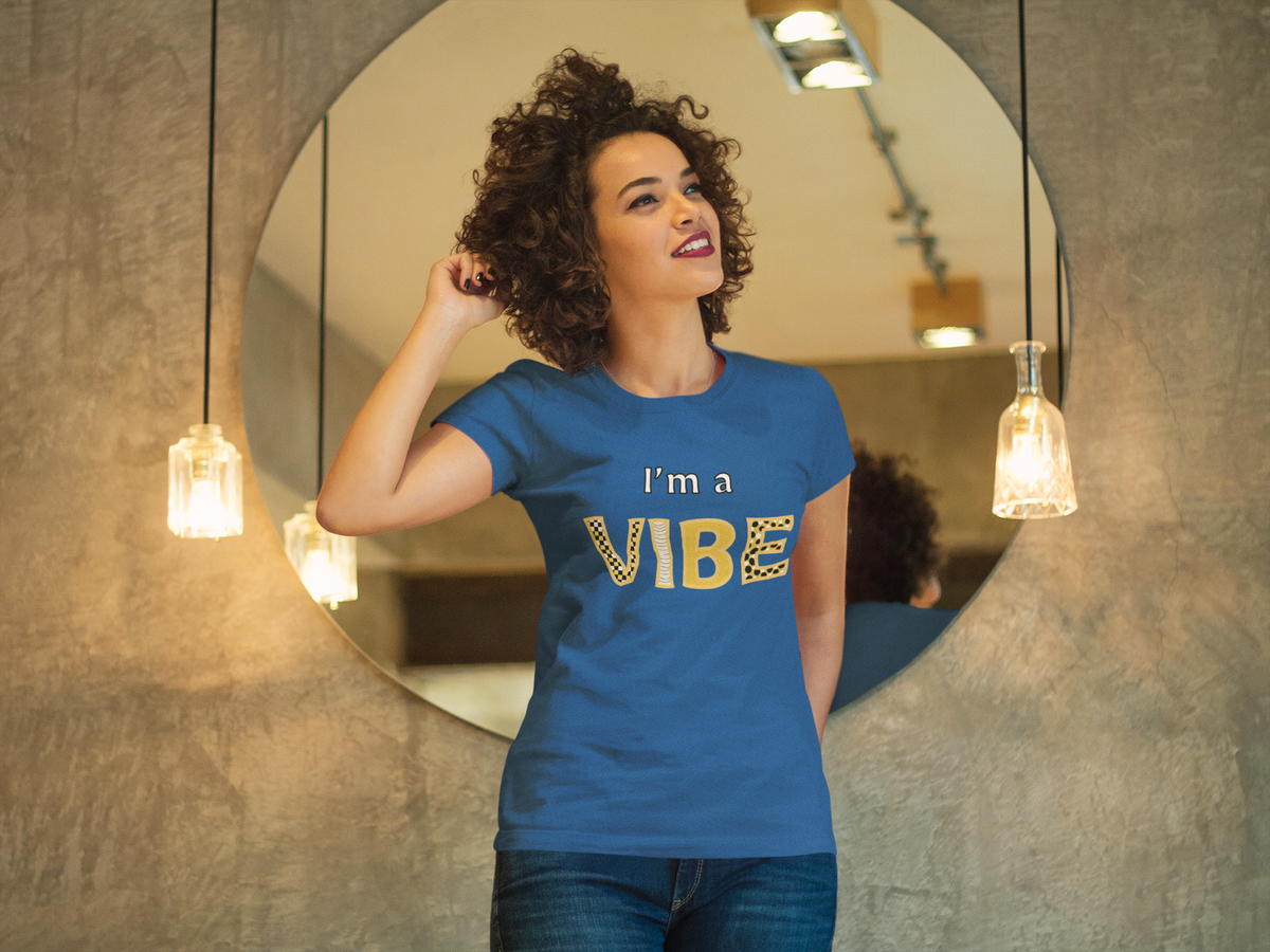 Smiling woman in the true royal I'm a Vibe tee stands in front of a round mirror.