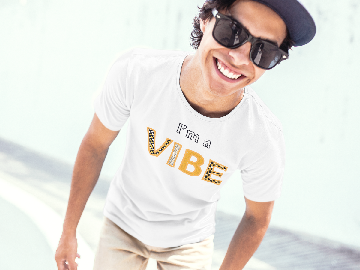 Smiling man in a backwards cap and sunglasses wears the white I'm a Vibe tee at a skatepark.