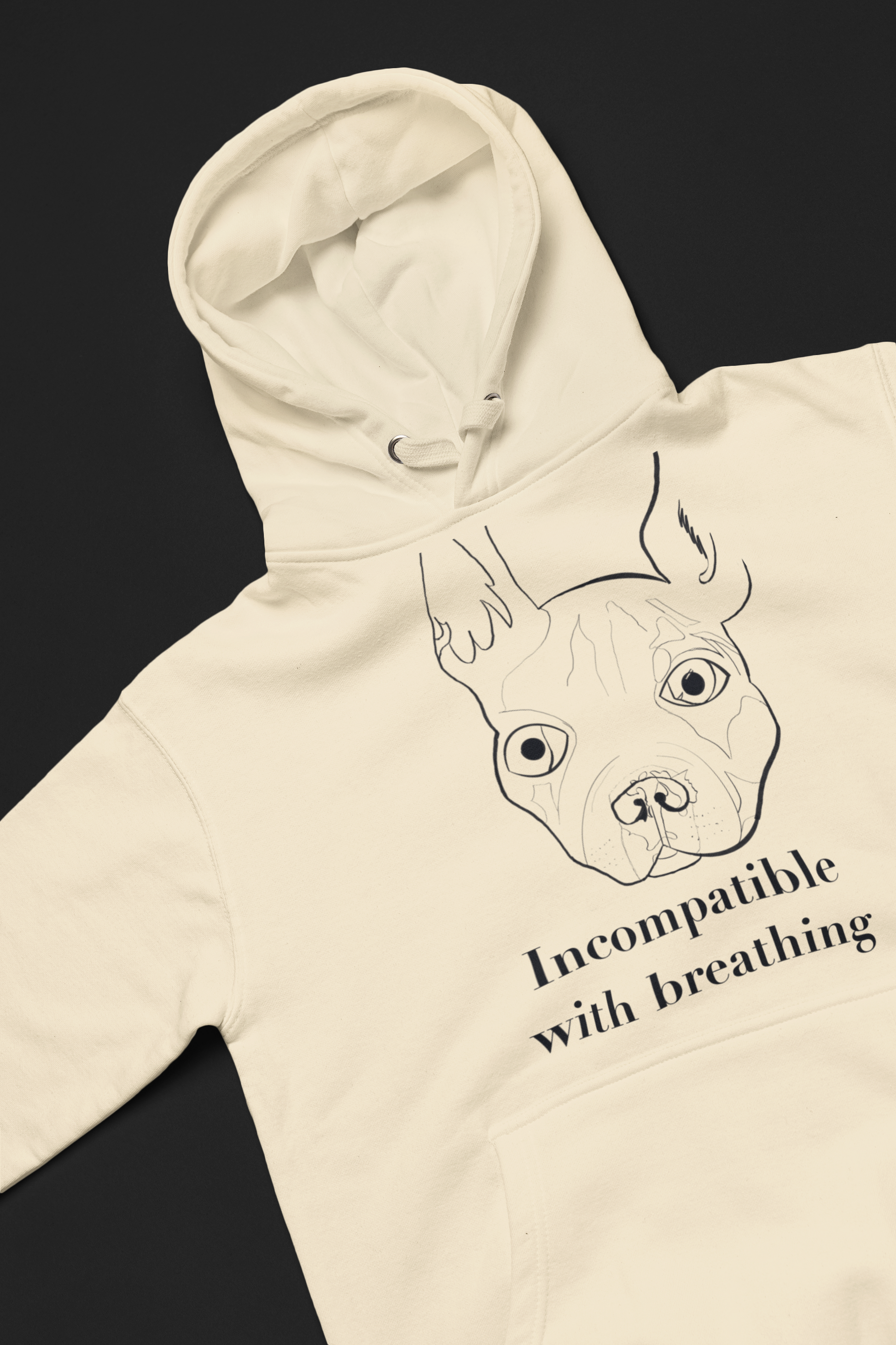 Bone color Cotton Heritage hoodie laid flat showing black ink French Bulldog design with "Incompatible with Breathing" text on chest