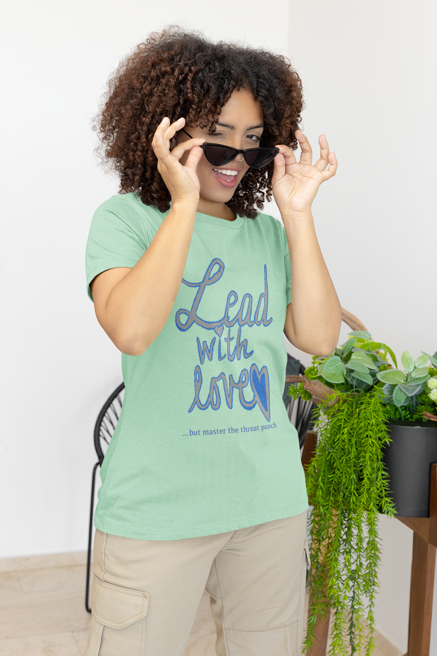 Woman taking off sunglasses wearing mint green Bella Canvas t-shirt with "Lead with Love… but master the throat punch" sarcastic self-care design. Empowering message for kind hearts with strong boundaries.