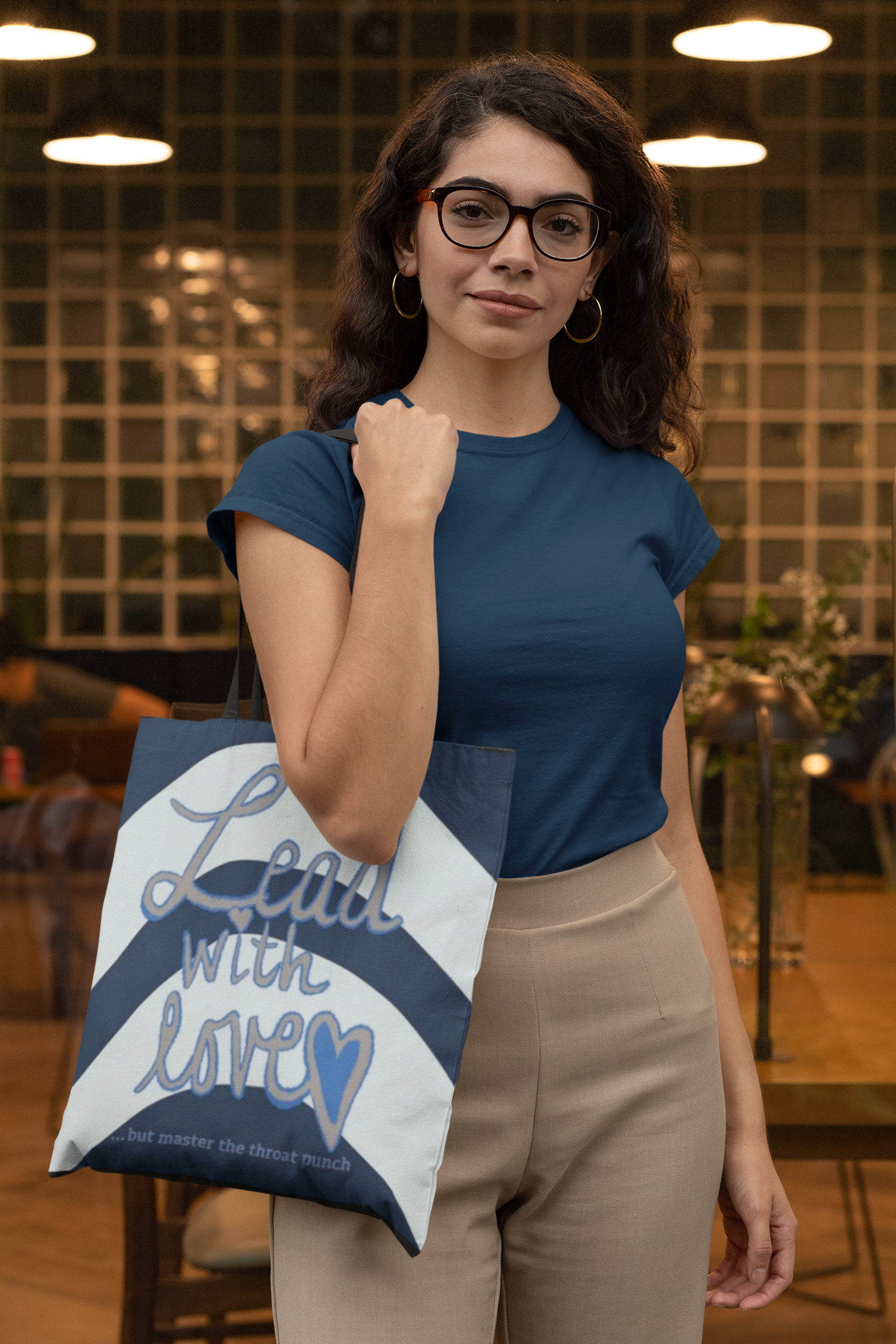 Woman in blue shirt showing back of all-over print tote bag with "Lead with Love… but master the throat punch" sarcastic self-care design. Versatile accessory for daily use and boundary-setting energy.