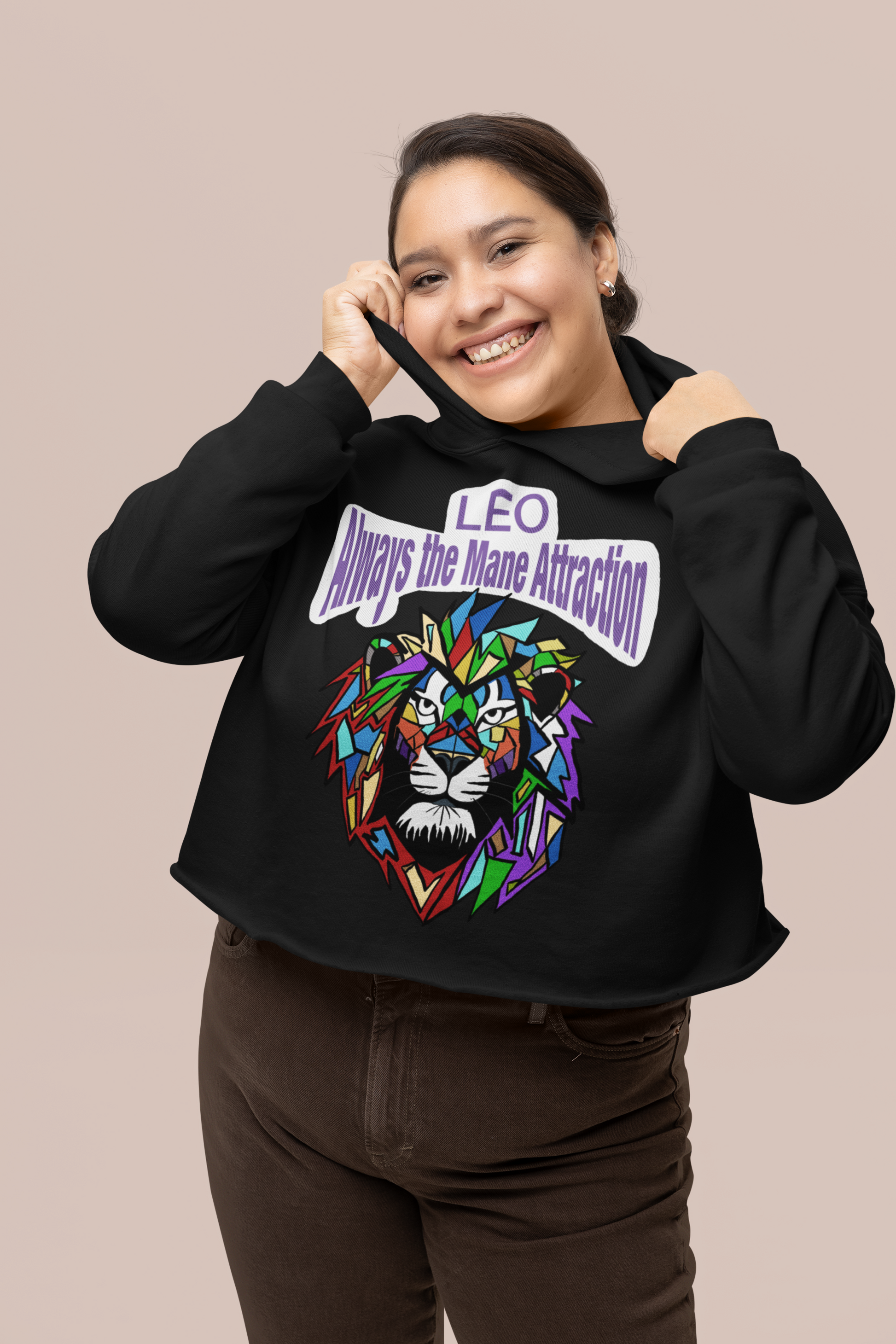 Smiling woman pulling the hood of a Black Bella + Canvas 7502 cropped hoodie featuring the Leo Always the Mane Attraction colorful lion design