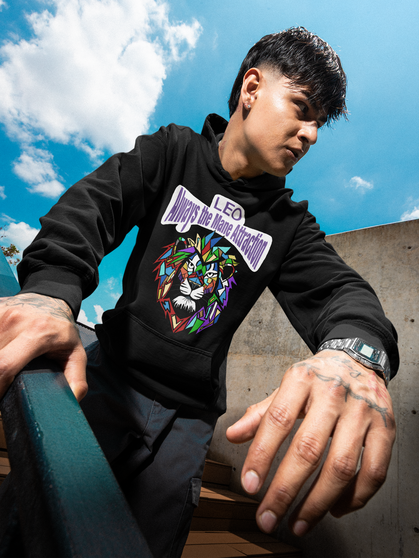 Tattooed man wearing a black Leo Always the Mane Attraction hoodie while walking down outdoor stadium stairs under a blue sky