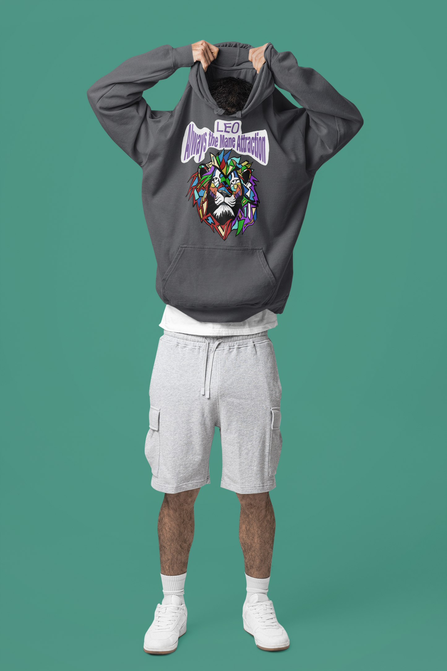 Man pulling a dark heather Leo Always the Mane Attraction hoodie over his head in a studio with a solid teal background