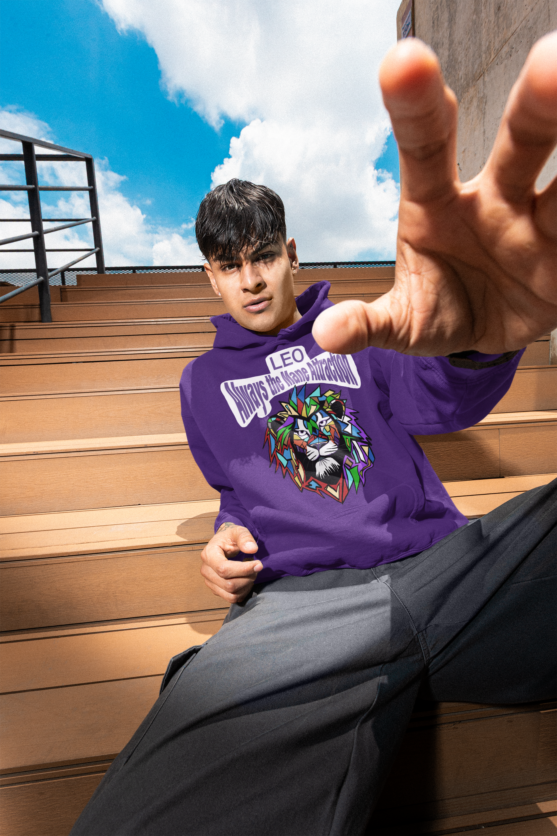 Young man in a purple Leo Always the Mane Attraction hoodie sitting on wooden bleachers and reaching his hand toward the camera