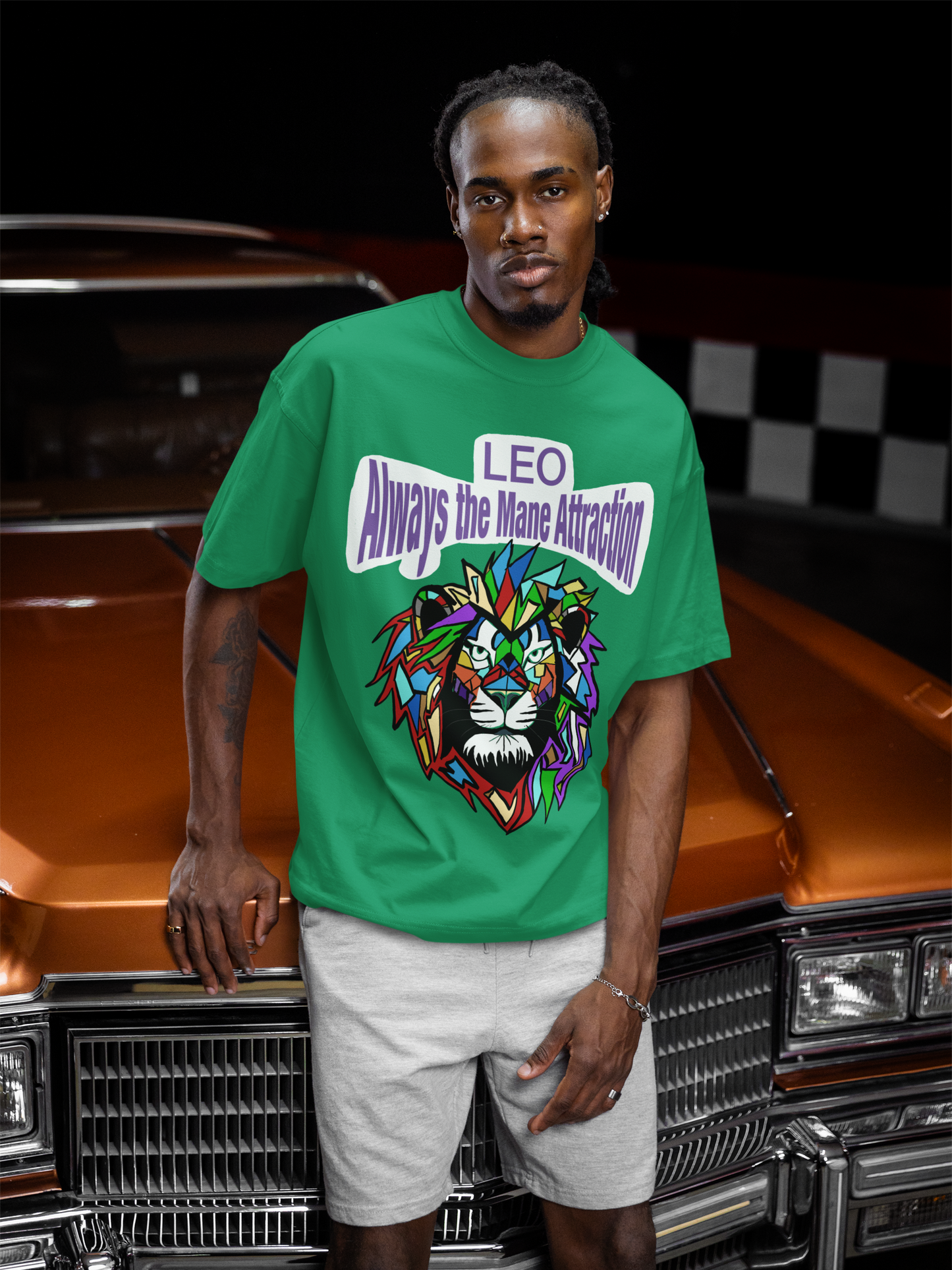 Man with braids posing against a classic orange car while wearing a kelly green Leo Always the Mane Attraction t-shirt