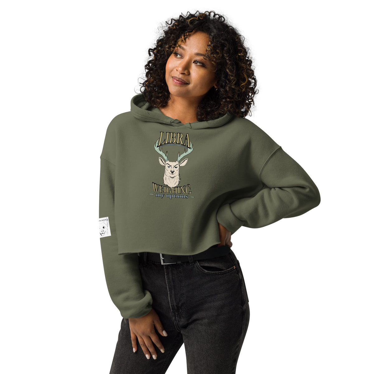 Woman with curly hair wearing a military green cropped Libra Weighing My Options hoodie, cream stag and gold lettering.