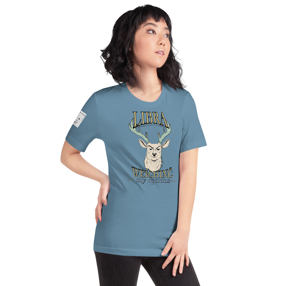Woman in a steel blue Libra Weighing My Options tee looking upward, cream stag and gold lettering on the chest, GrungePup logo on the right sleeve.