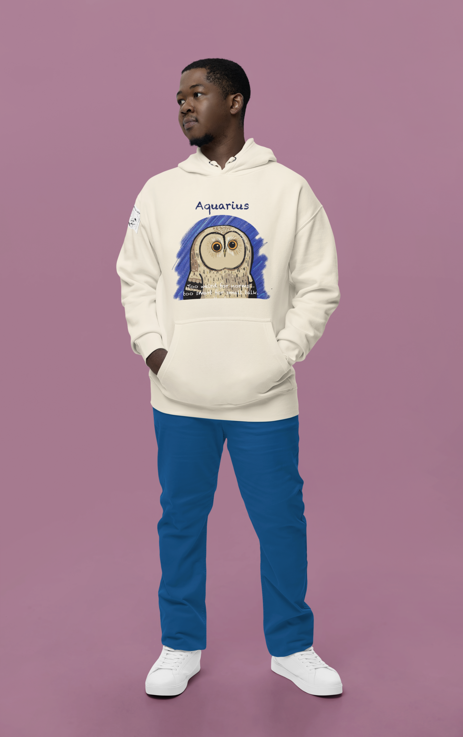 Man standing against a pink background wearing an oatmeal heather Cotton Heritage hoodie with the Aquarius Owl artwork by GrungePup