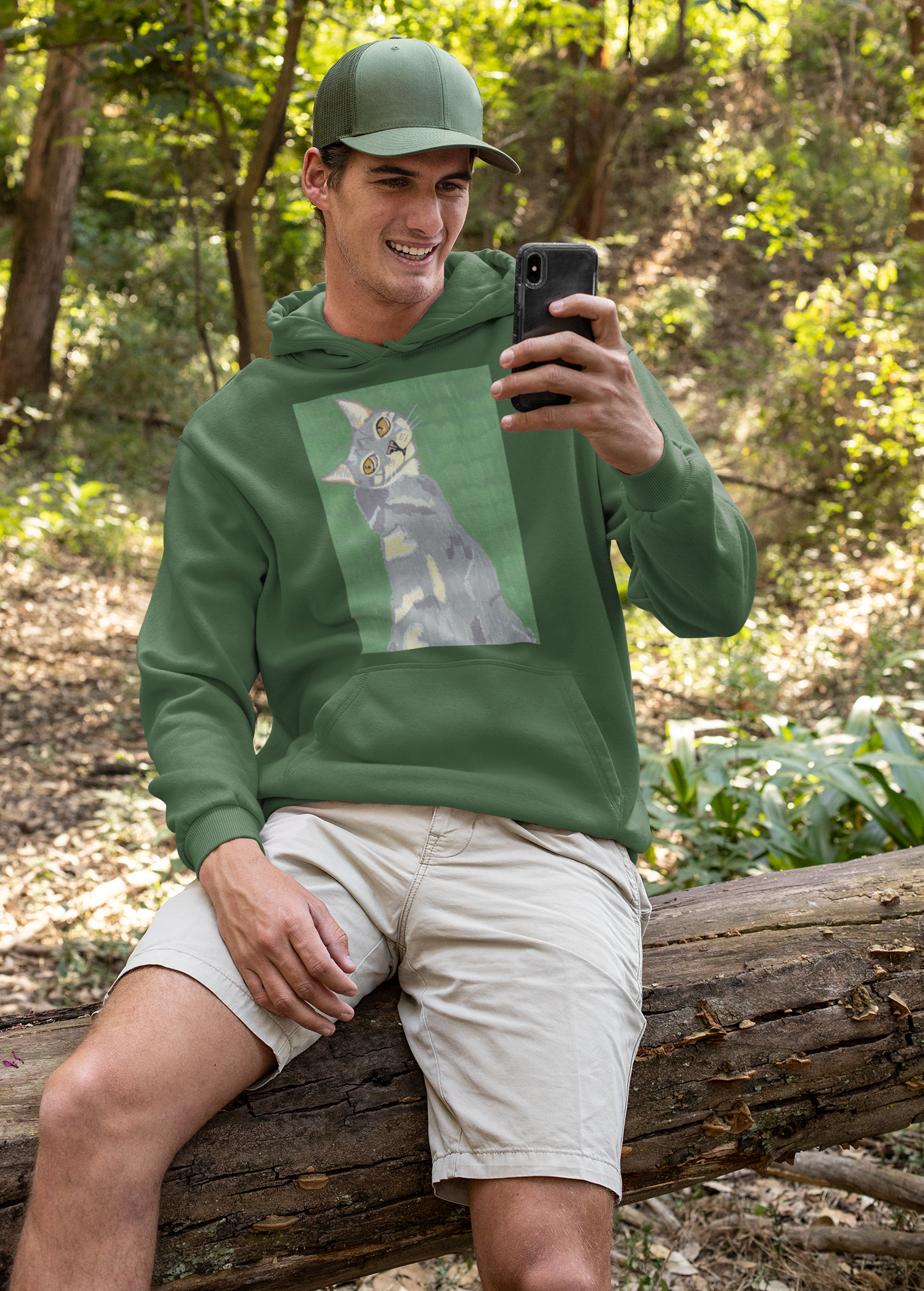 Smiling man sitting on a log in the woods wearing a forest green hoodie with Mr. Grey cat portrait by GrungePup