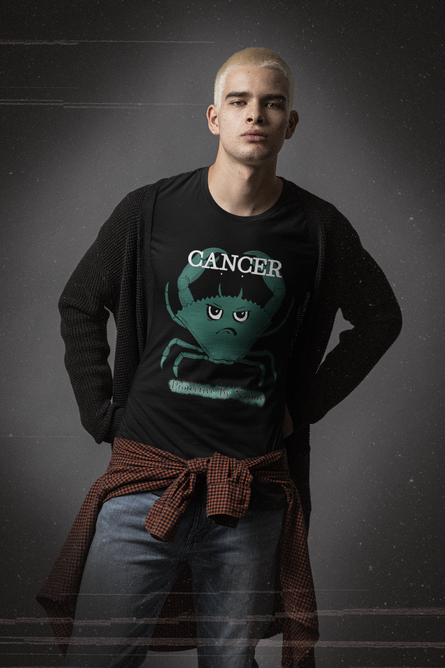 Man with platinum blonde hair wearing a black heather Cancer "Protective By Nature" t-shirt layered under a black cardigan, standing in a moody studio