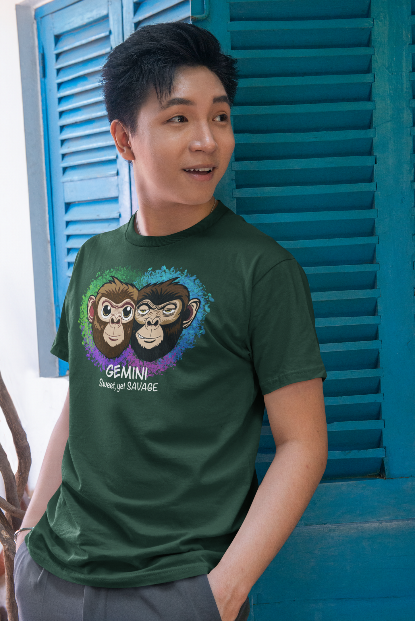Man with short black hair wearing a forest green Gemini "Sweet, yet SAVAGE" t-shirt, standing against a bright blue door outdoors