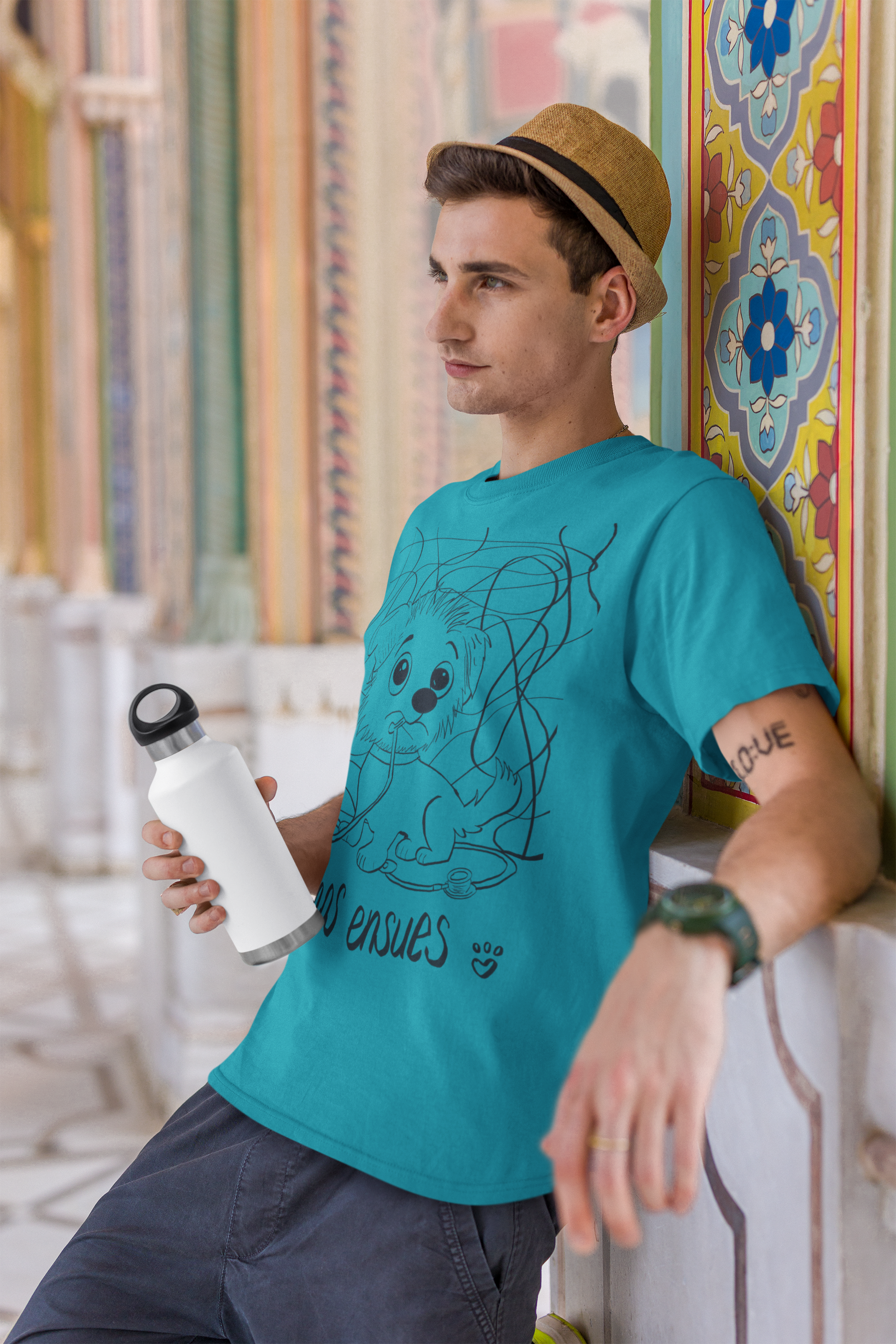 Young man wearing turquoise Chaos Ensues t-shirt holding a white water bottle outdoors