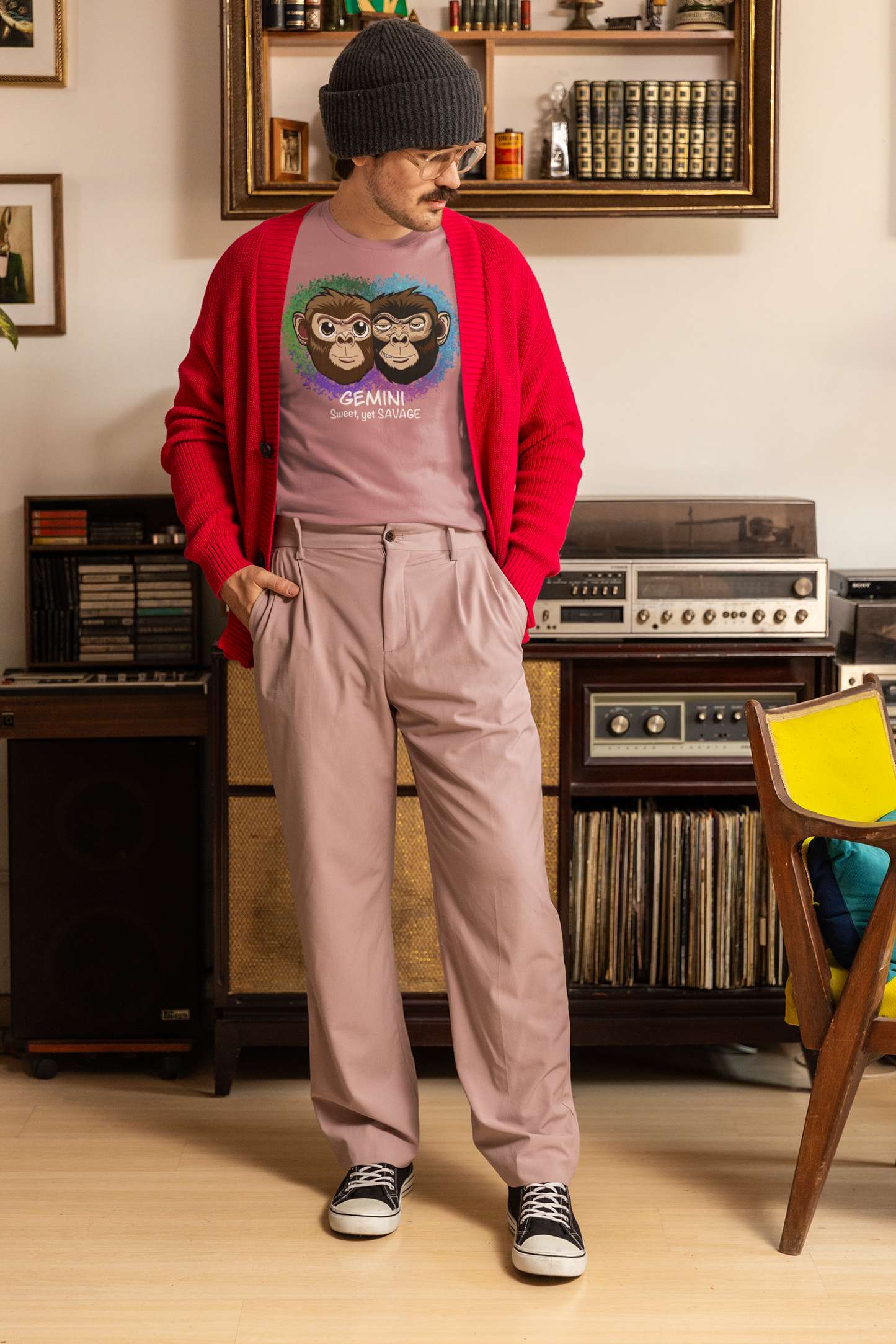 Man with beanie and glasses wearing a heather orchid Gemini "Sweet, yet SAVAGE" t-shirt under a red cardigan in a vintage room
