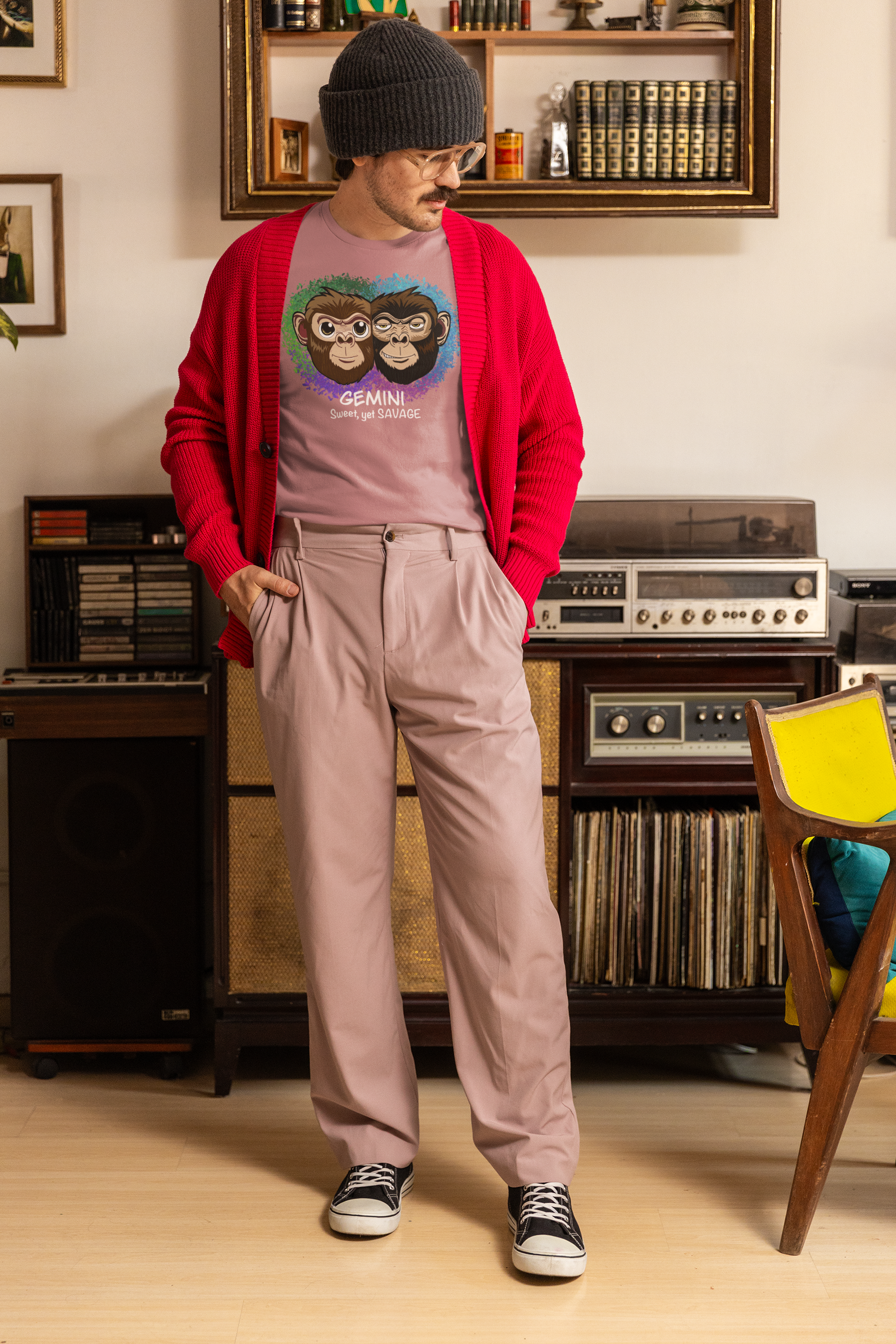 Man with beanie and glasses wearing a heather orchid Gemini "Sweet, yet SAVAGE" t-shirt under a red cardigan in a vintage room