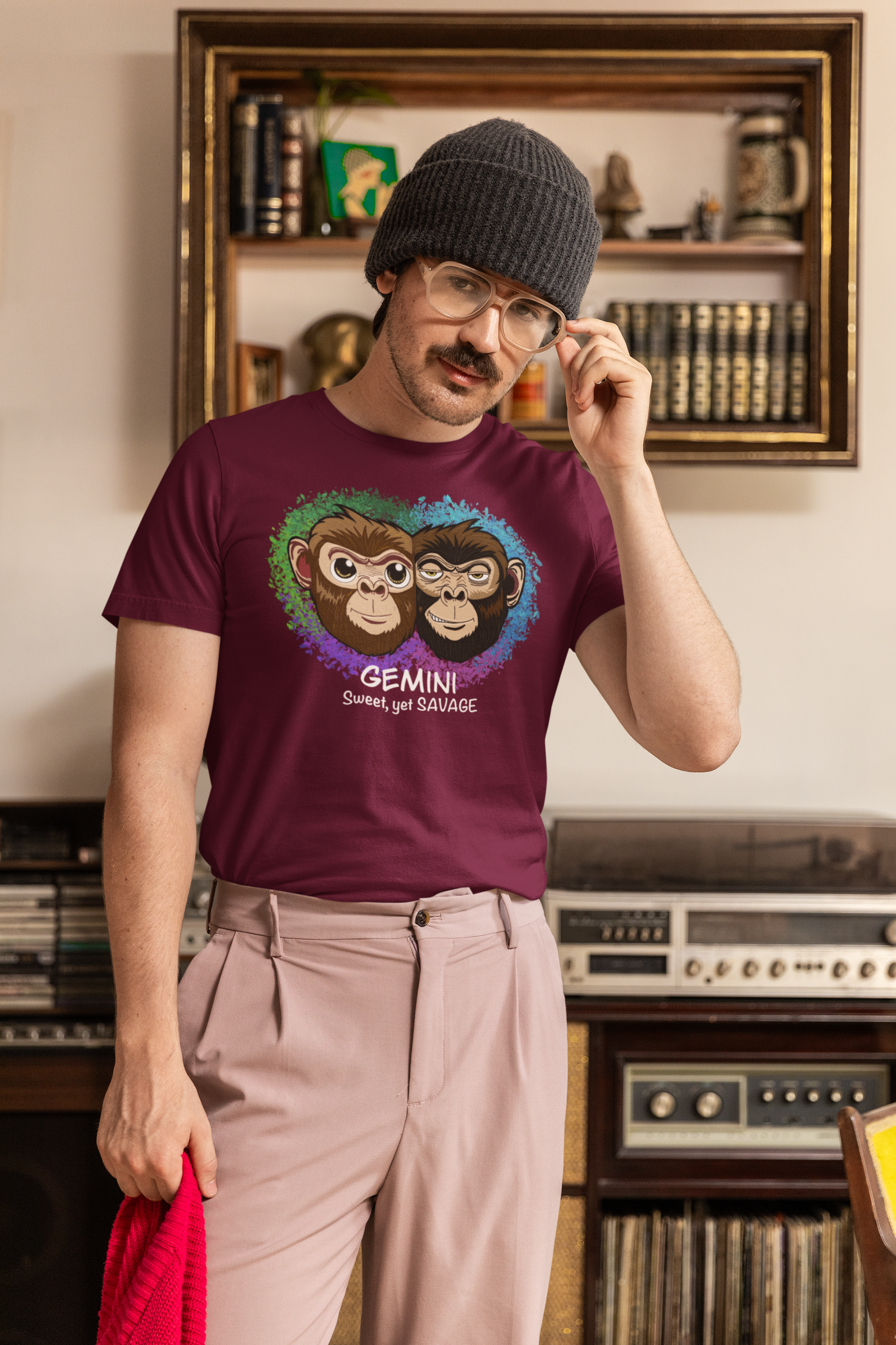 Man with glasses and beanie wearing a maroon Gemini "Sweet, yet SAVAGE" t-shirt, posing in front of bookshelves
