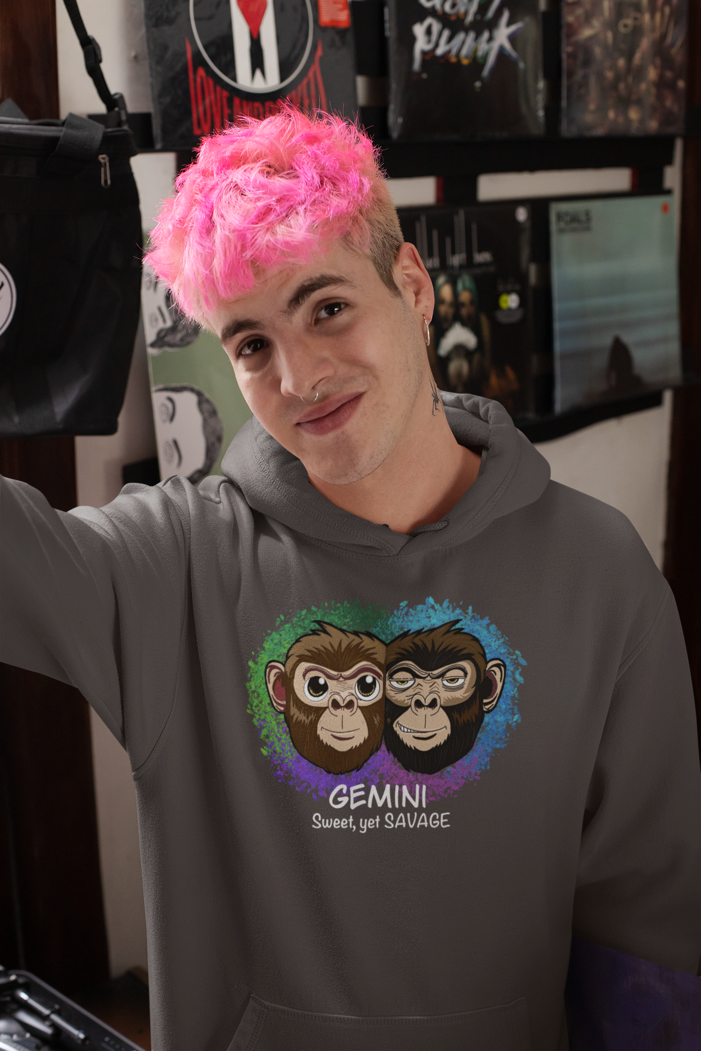 Man with bright pink hair wearing a charcoal heather Gemini "Sweet, yet SAVAGE" hoodie browsing records in a music store