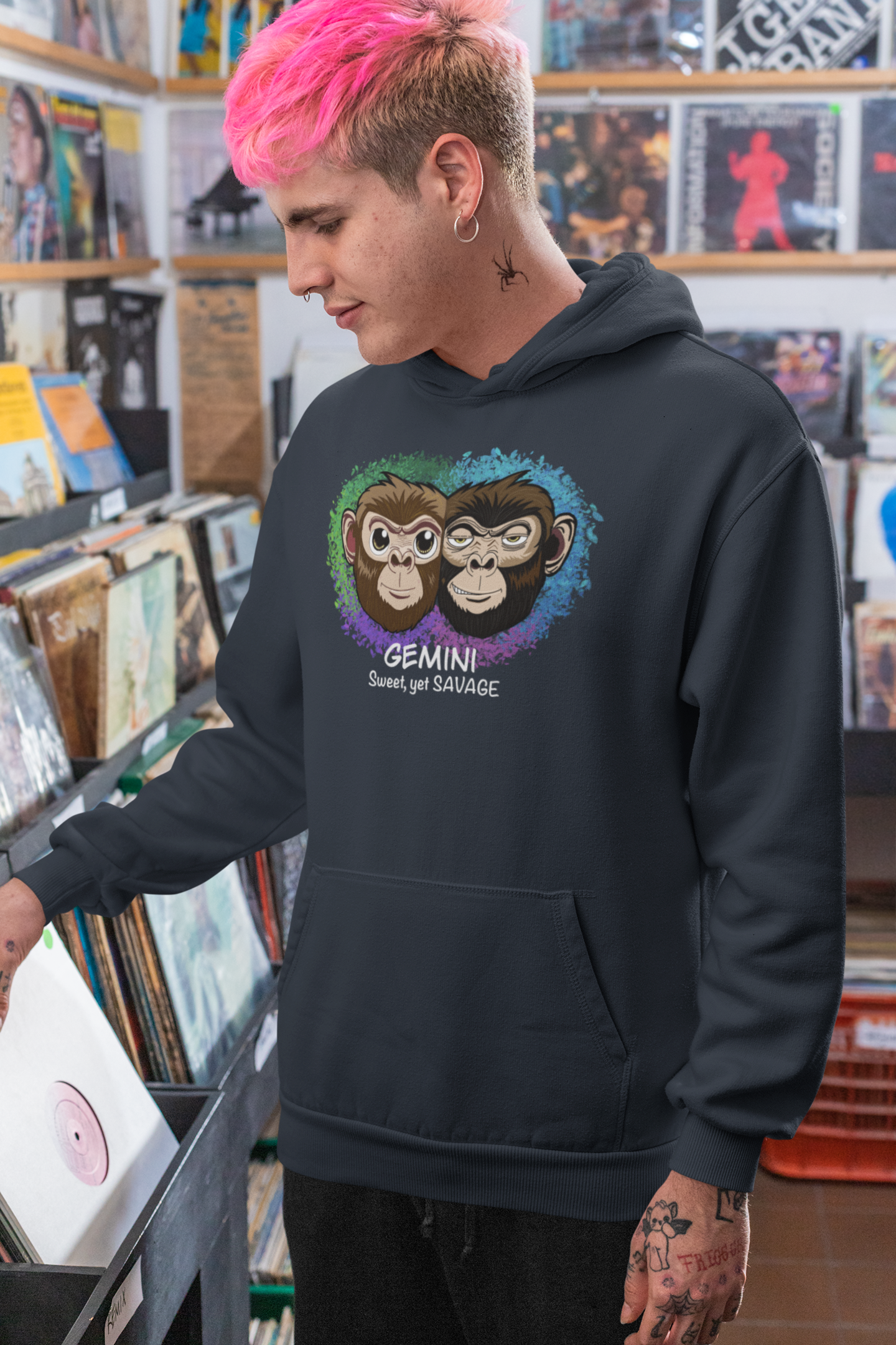 Man with bright pink hair wearing a navy blazer blue Gemini "Sweet, yet SAVAGE" hoodie, posing in a music store