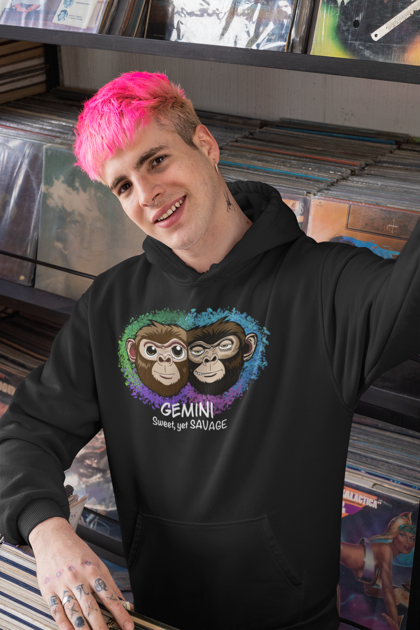 Man with bright pink hair smiling and taking a selfie while wearing a black Gemini "Sweet, yet SAVAGE" hoodie in a record store