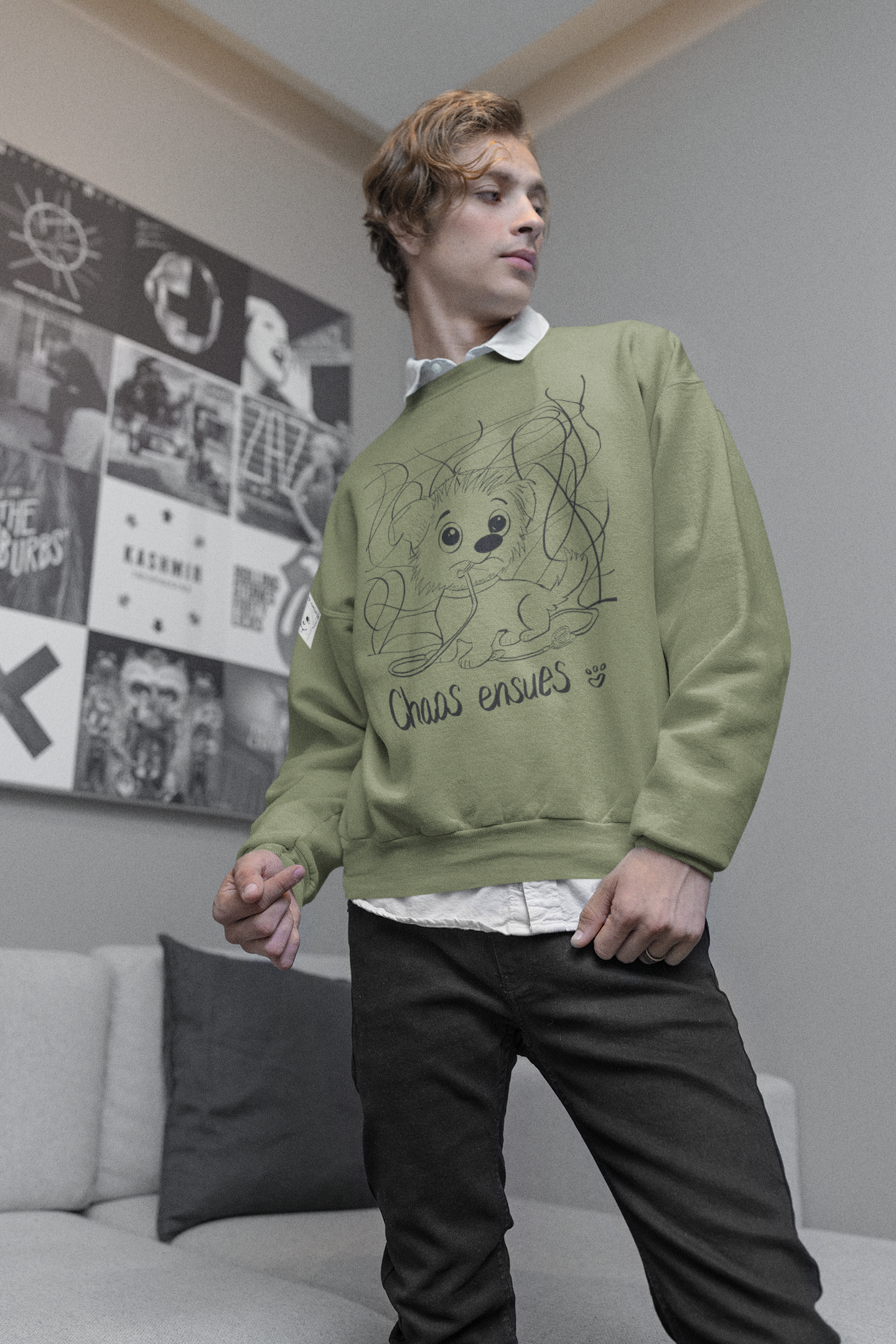 Young man with brown wavy hair wearing an olive green Chaos Ensues sweatshirt standing in a modern living room