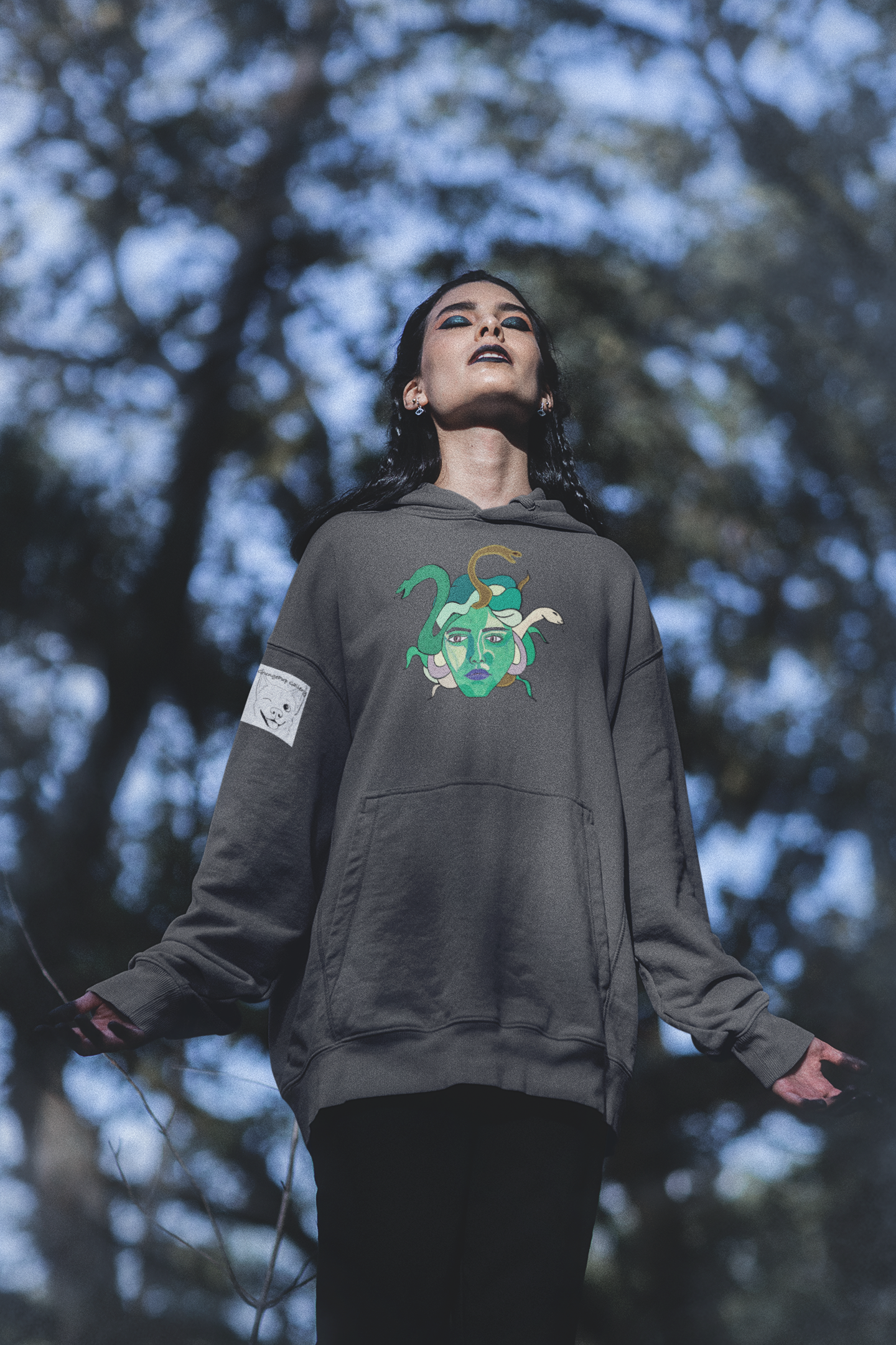 Woman standing in a forest with arms open, wearing an asphalt Medusa hoodie by GrungePup Gallery