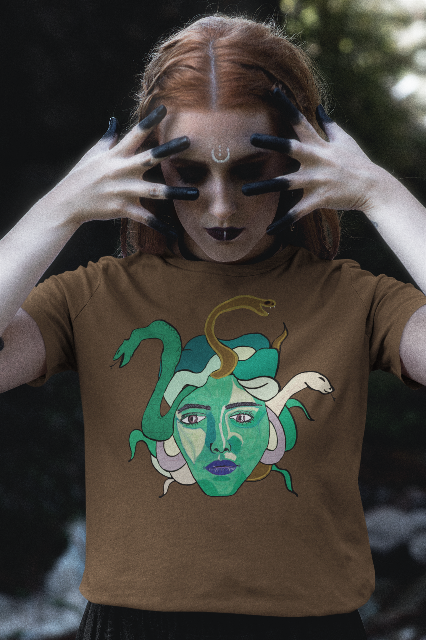 Redheaded woman with painted fingers framing her face, wearing a heather brown Medusa t-shirt by GrungePup Gallery