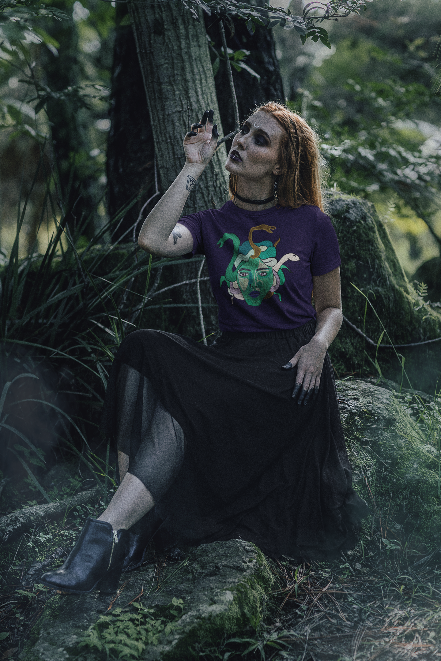 Woman sitting on a mossy rock in the forest, wearing a team purple Medusa t-shirt by GrungePup Gallery